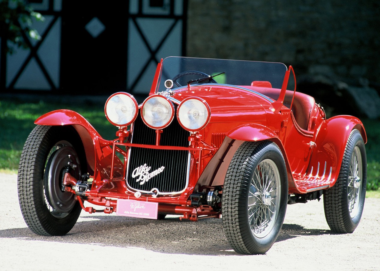 Alfa Romeo 8C modèle 1931 avec 3 feux à l'avant, de couleur rouge stationnée devant une propriété.