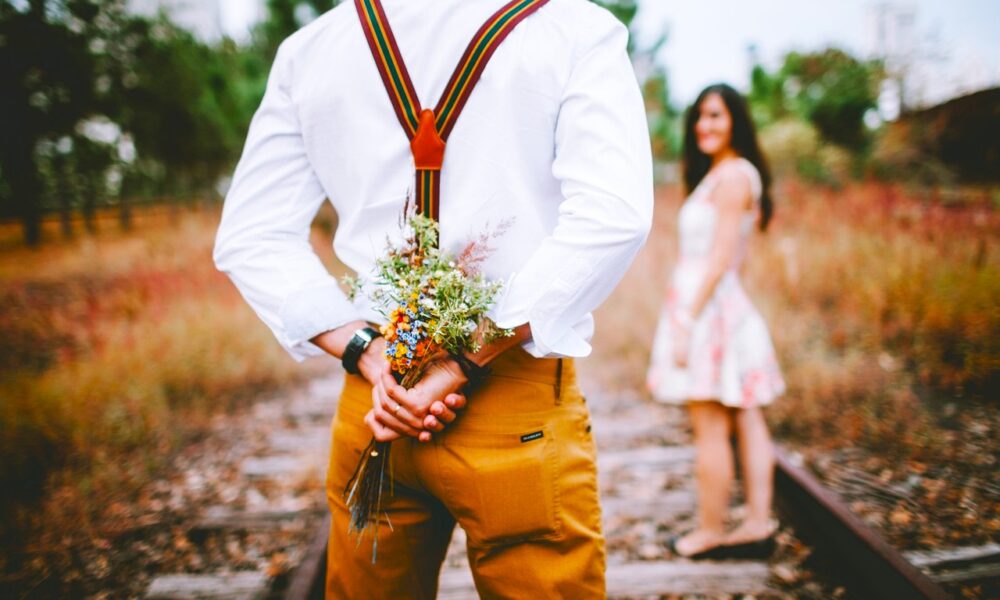 Homme vintage en bretelles qui cache un bouquet de fleurs pour l'offrir à sa fiancée
