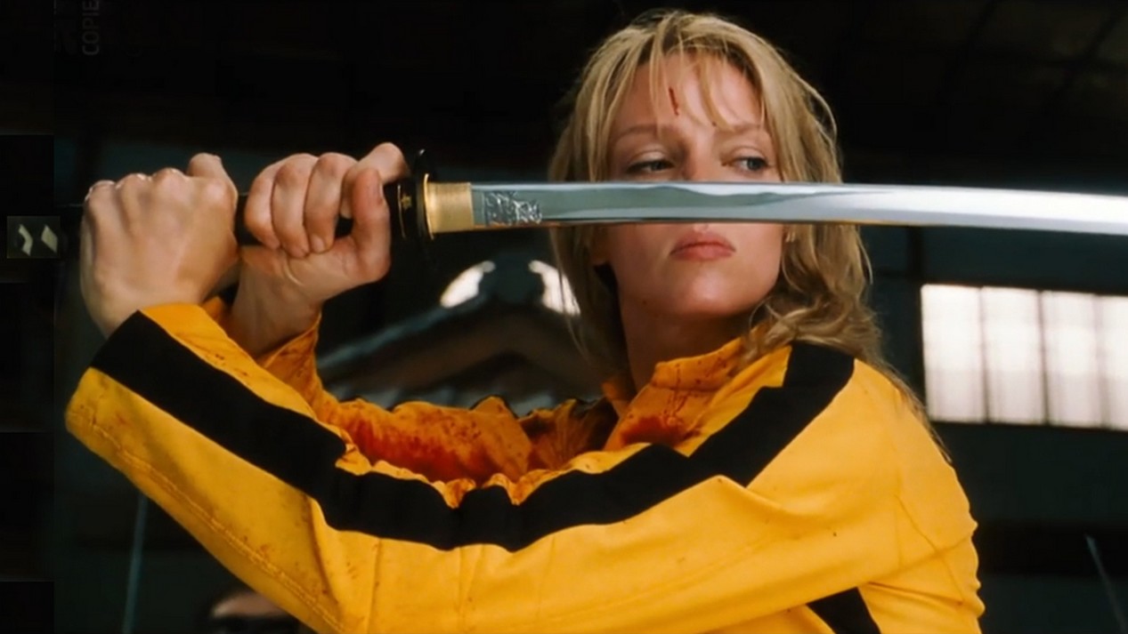 L'actrice Uma Thurman vêtue d'une combinaison jaune à bandes noires, référence à Bruce Lee, dans le film KILL BILL VOLUME 1, avec un sabre.