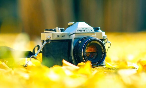 Appareil photo argentique de la marque japonaise Pentax : le modèle Pentax K1000, posé dans des feuilles d'automne, un modèle sorti en 1976 et stoppé en 1997