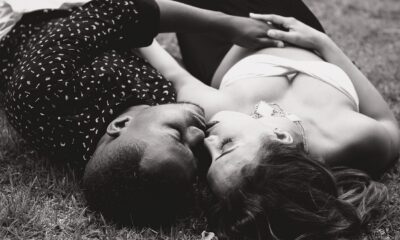 Une femme blanche et un homme noir allongés dans l'herbe en train de s'embrasser