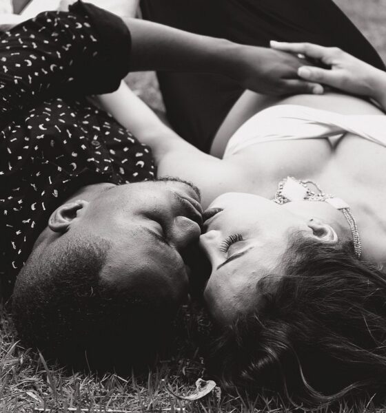 Une femme blanche et un homme noir allongés dans l'herbe en train de s'embrasser