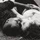 Une femme blanche et un homme noir allongés dans l'herbe en train de s'embrasser