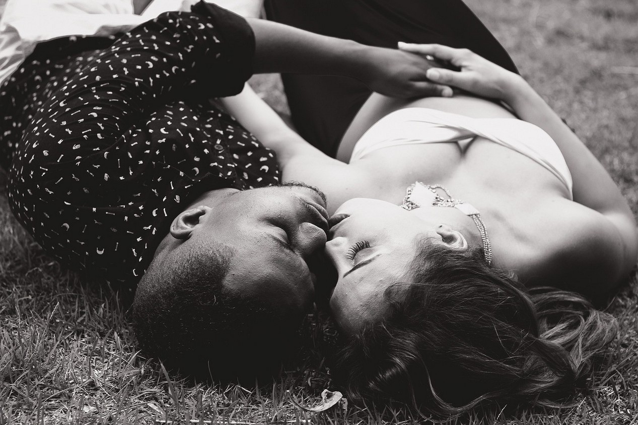 Une femme blanche et un homme noir allongés dans l'herbe en train de s'embrasser