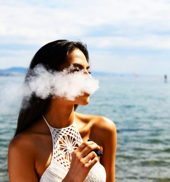 Femme avec un haut blanc sans manches qui fume une cigarette électronique