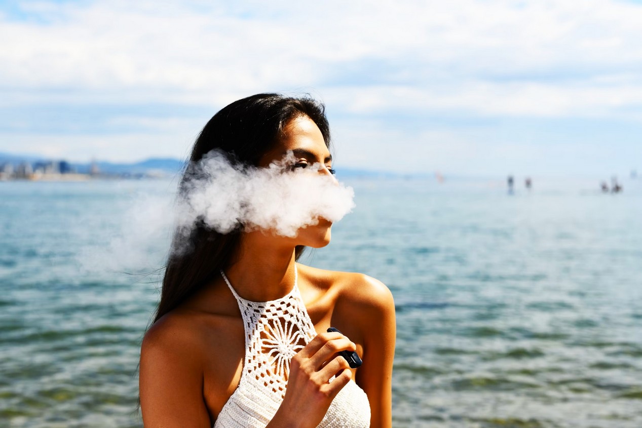 Femme avec un haut blanc sans manches qui fume une cigarette électronique