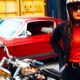 Femme portant les vêtements pour moto de la marque française Wildust Sisters, avec une moto noire et une auto rouge vintage