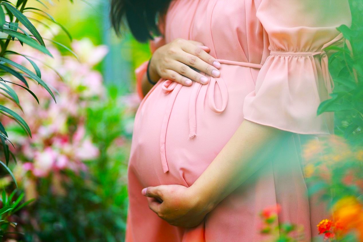 Femme enceinte portant une robe rose entourée de fleurs