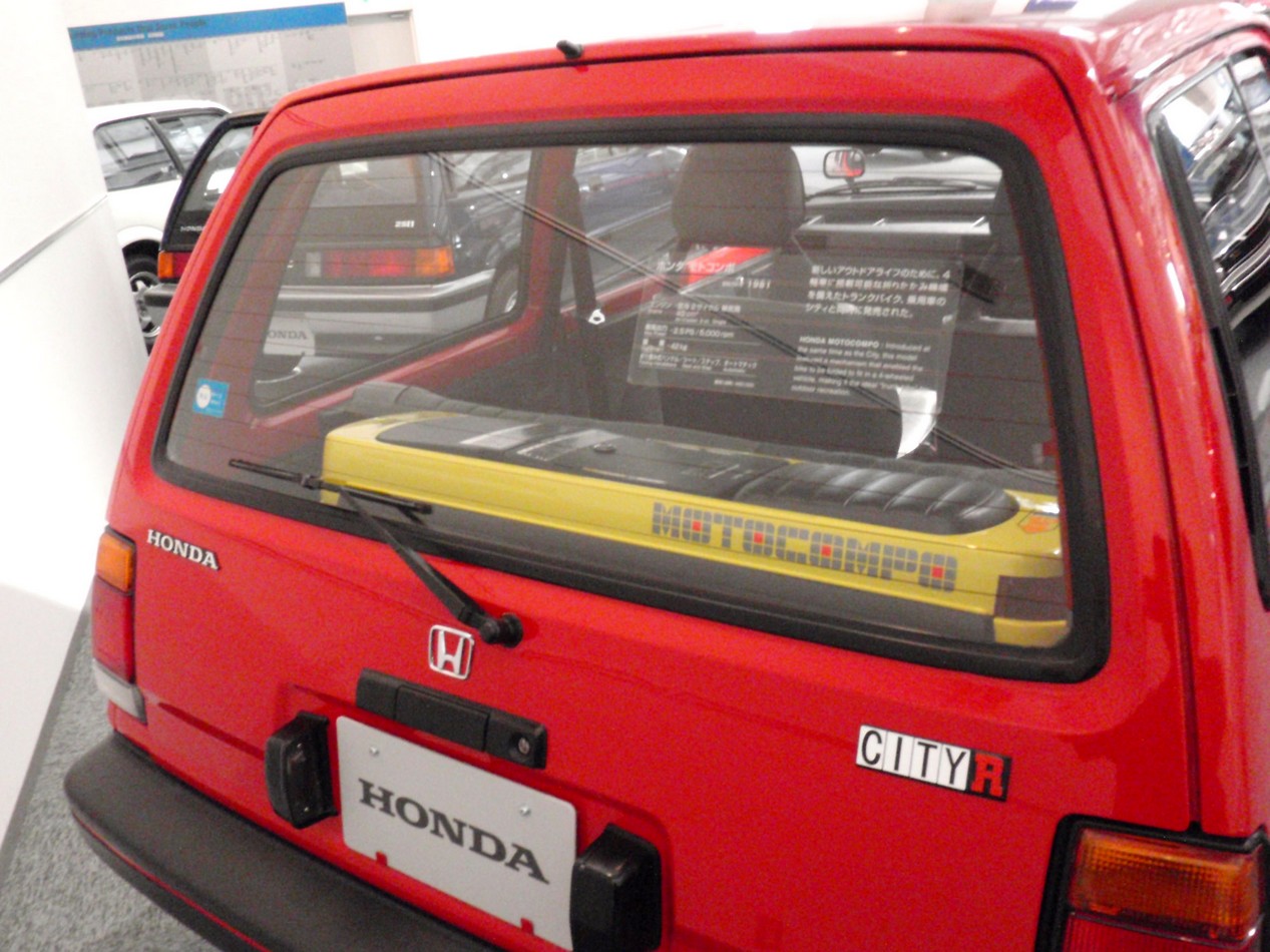 Voiture Honda City rouge avec un scooter pliable Motocompo dans le coffre
